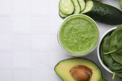 Tasty green smoothie in glass and products on white tiled table, flat lay. Space for text