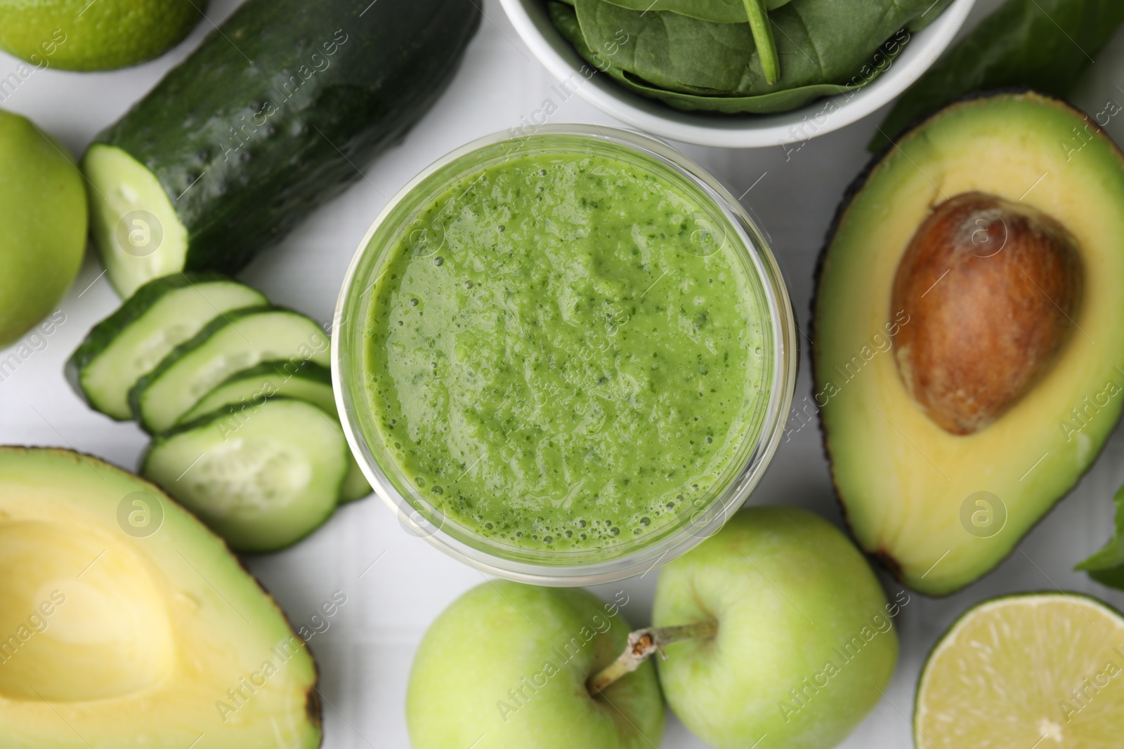 Photo of Tasty green smoothie in glass and products on white tiled table, flat lay