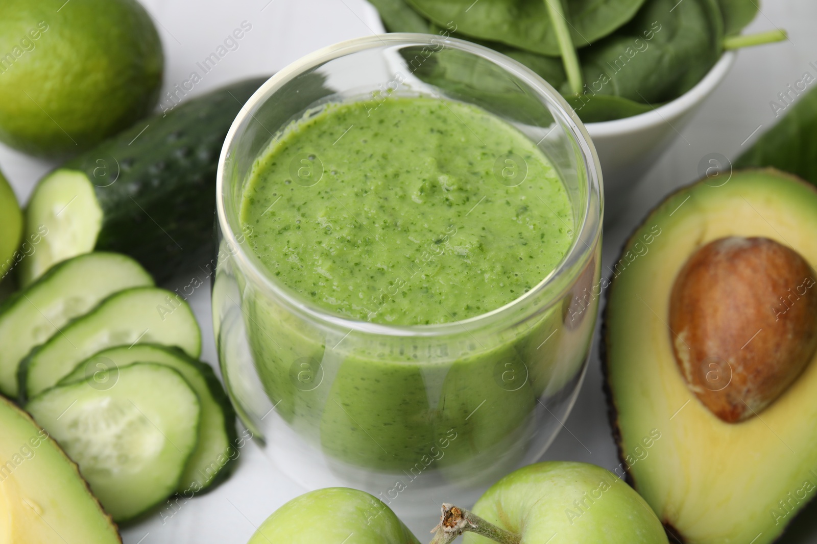 Photo of Tasty green smoothie in glass and products on white table, closeup