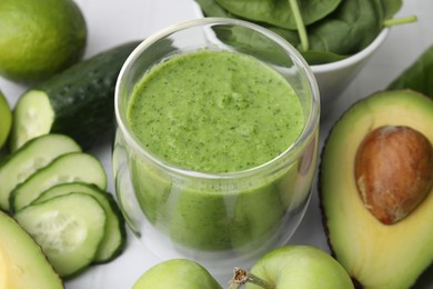 Photo of Tasty green smoothie in glass and products on white table, closeup