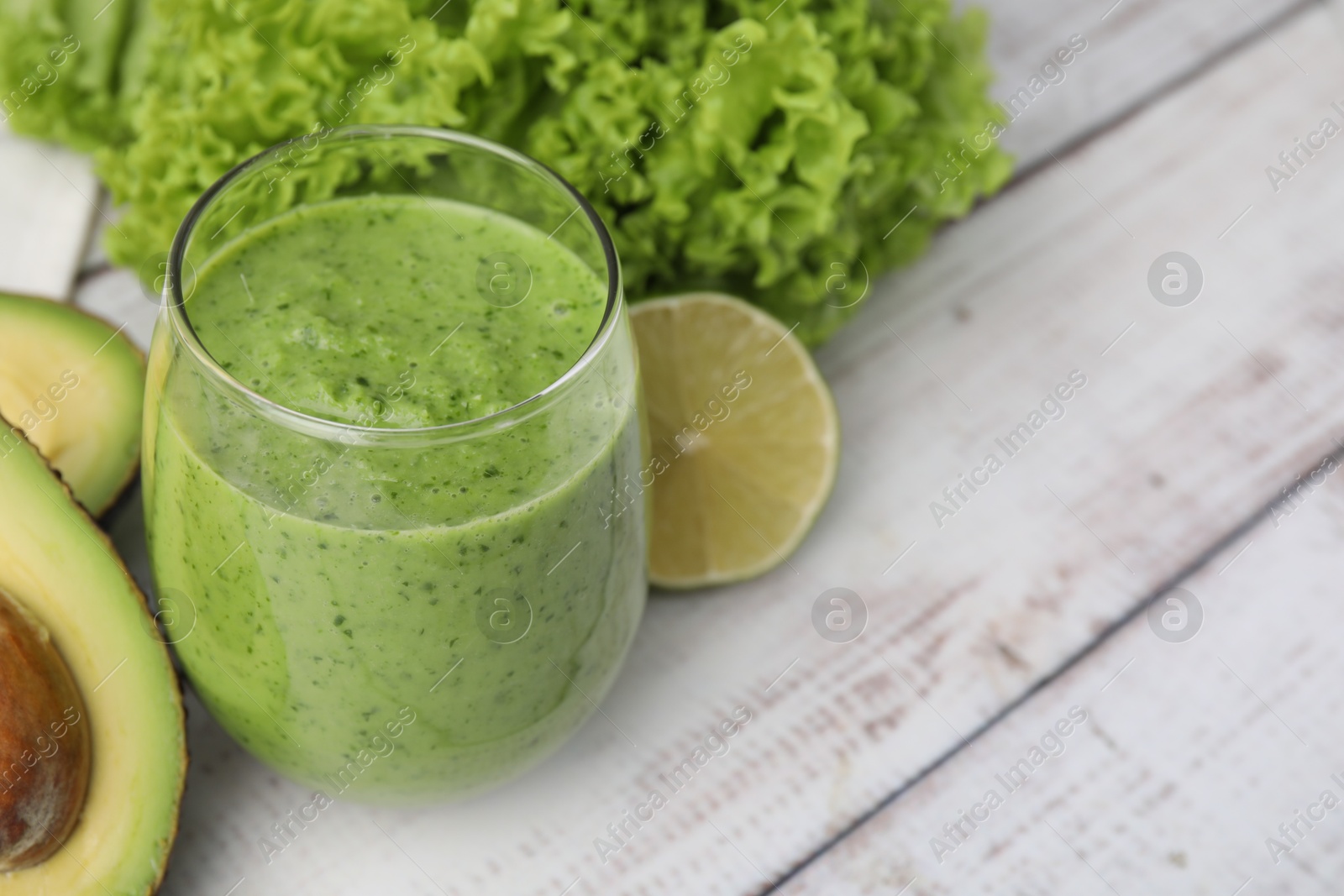 Photo of Tasty green smoothie in glass and products on wooden rustic table, closeup. Space for text