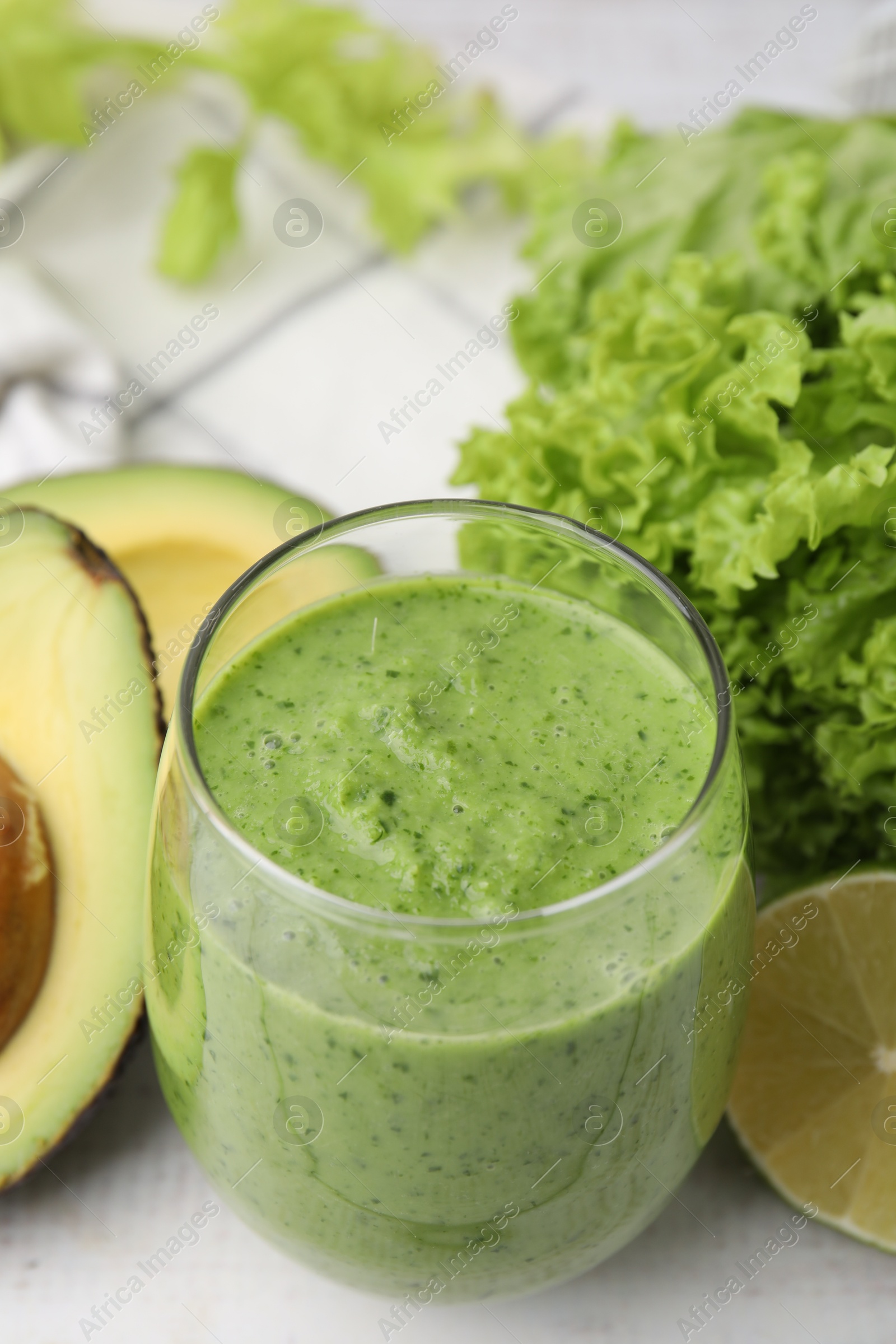 Photo of Tasty green smoothie in glass and products on white table, closeup