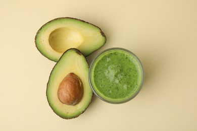 Photo of Tasty green smoothie in glass and halves of avocado on beige background, flat lay