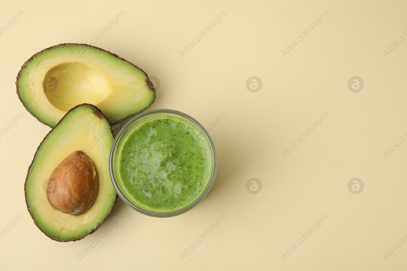 Photo of Tasty green smoothie in glass and halves of avocado on beige background, flat lay. Space for text