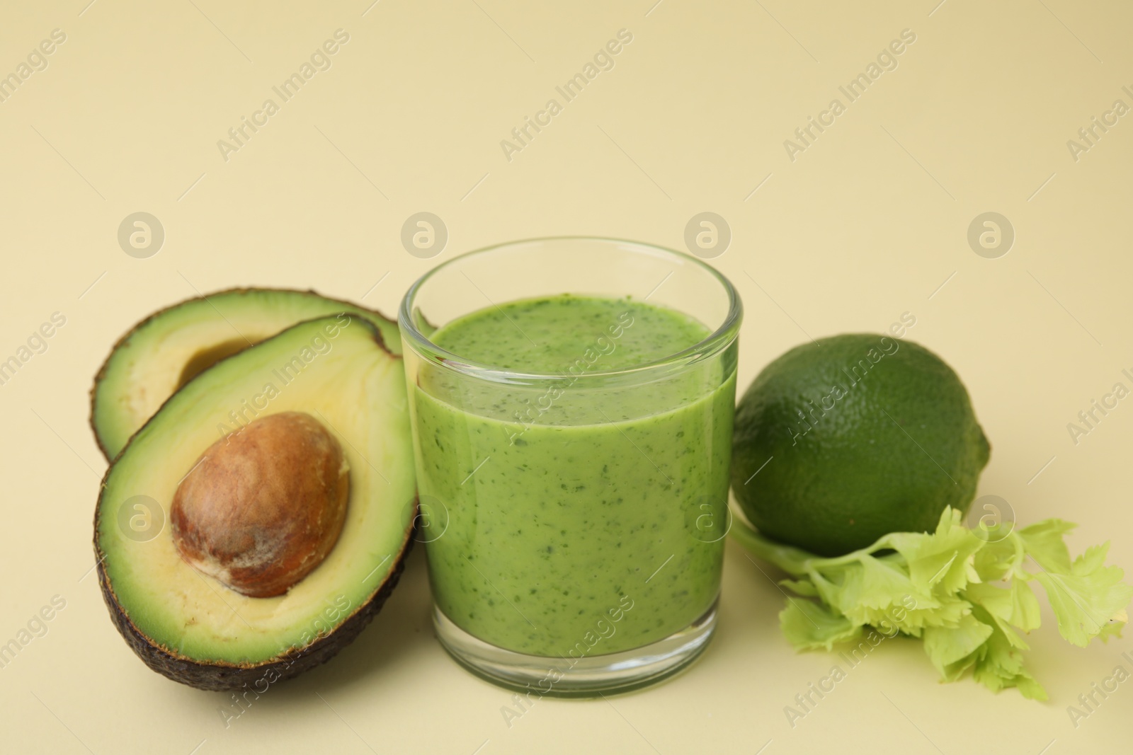 Photo of Tasty green smoothie in glass and products on beige background, closeup