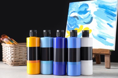 Photo of Acrylic paints of different colors in bottles and small easel with abstract picture on light table