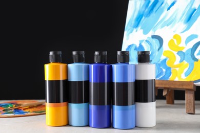 Acrylic paints of different colors in bottles and small easel with abstract picture on light table