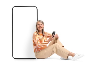 Happy mature woman holding mobile phone and sitting near big smartphone on white background