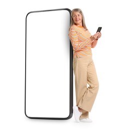 Image of Happy mature woman holding mobile phone near big smartphone on white background