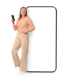 Image of Happy mature woman holding mobile phone near big smartphone on white background