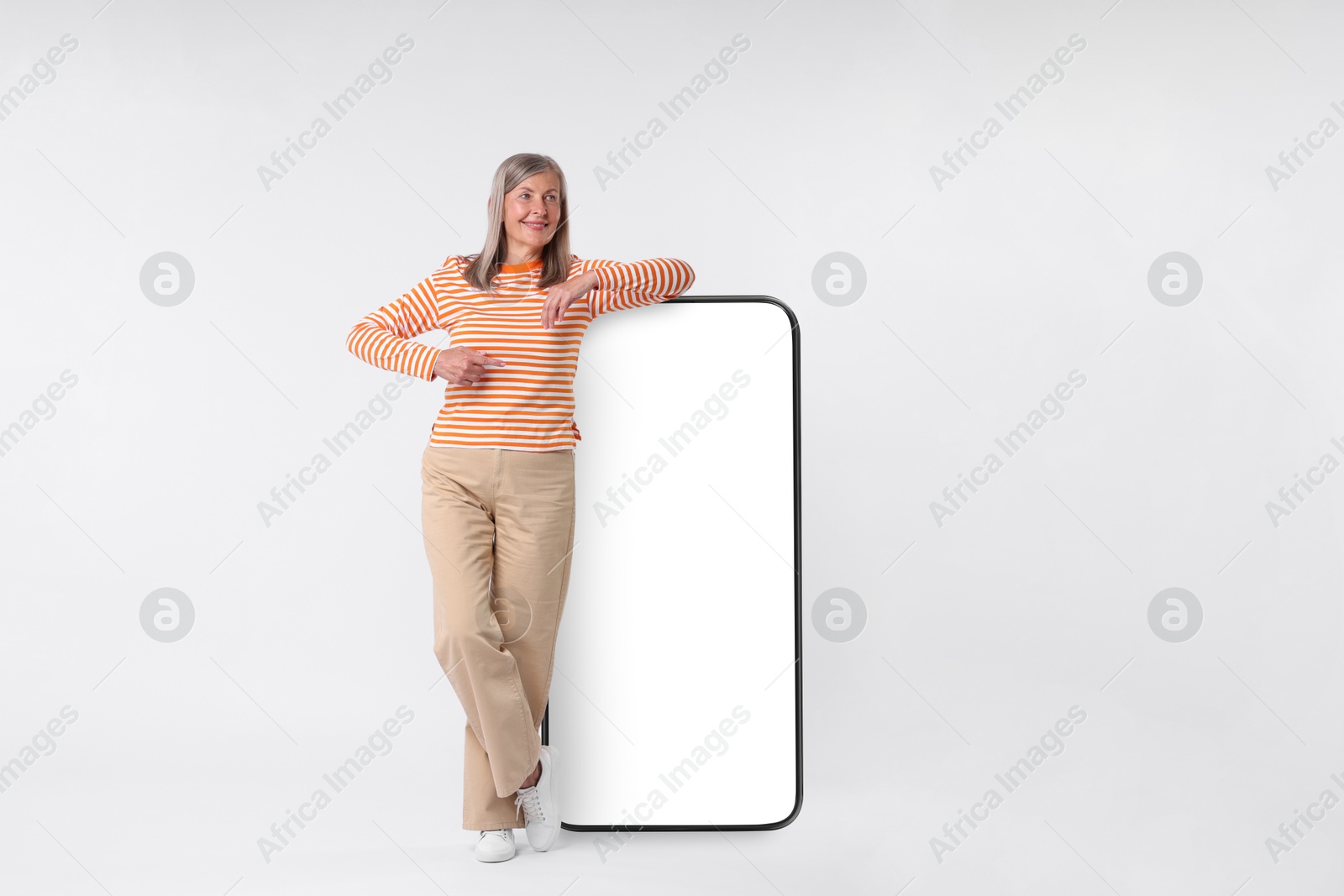 Image of Happy mature woman pointing at big mobile phone on white background