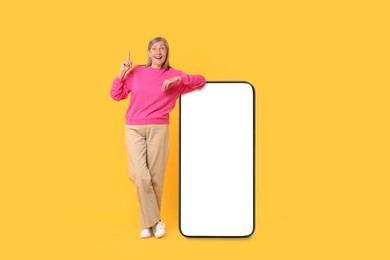 Image of Happy mature woman leaning on big mobile phone against orange background