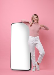 Image of Happy woman pointing at big mobile phone on pink background