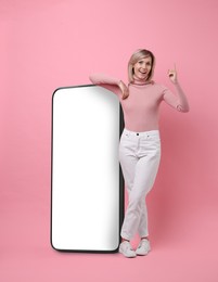 Image of Happy woman leaning on big mobile phone against pink background