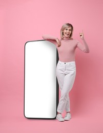 Happy woman leaning on big mobile phone against pink background