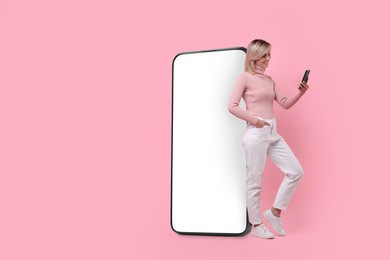 Happy woman holding mobile phone near big smartphone on pink background