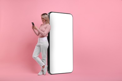 Image of Happy woman holding mobile phone near big smartphone on pink background