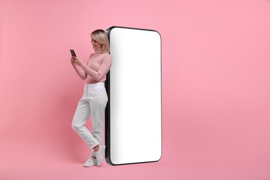 Happy woman holding mobile phone near big smartphone on pink background