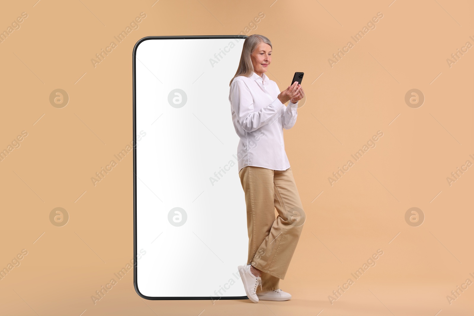 Image of Happy mature woman holding mobile phone near big smartphone on dark beige background