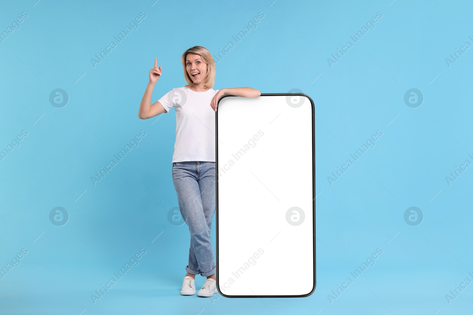 Image of Happy woman leaning on big mobile phone against light blue background