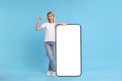 Happy woman leaning on big mobile phone against light blue background