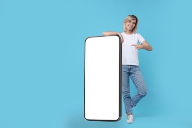 Happy woman pointing at big mobile phone on light blue background