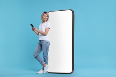 Image of Happy woman holding mobile phone near big smartphone on light blue background