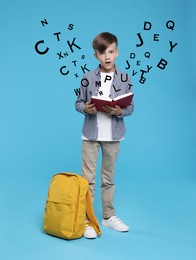 Surprised boy with book and backpack on light blue background. Letters flying out of book