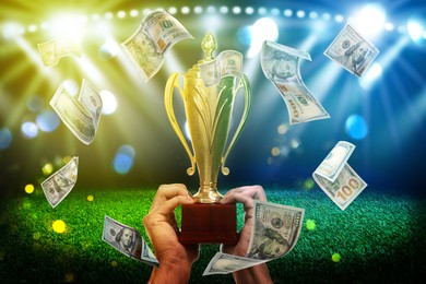 Image of Man holding gold trophy cup in money rain at stadium, closeup