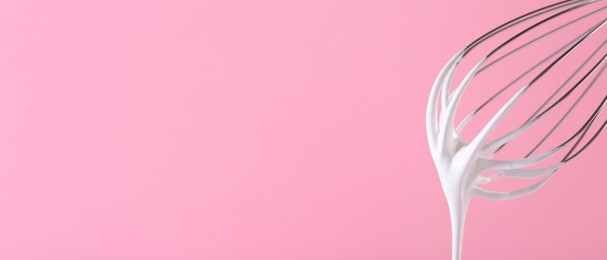 Image of Whisk with beaten cream on pink background, closeup. Banner design, space for text