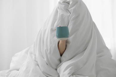 Woman wrapping in blanket sitting with cup of coffee at home. Good morning