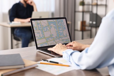 Photo of Smiling cartographer working with cadastral map on laptop at wooden table in office, closeup