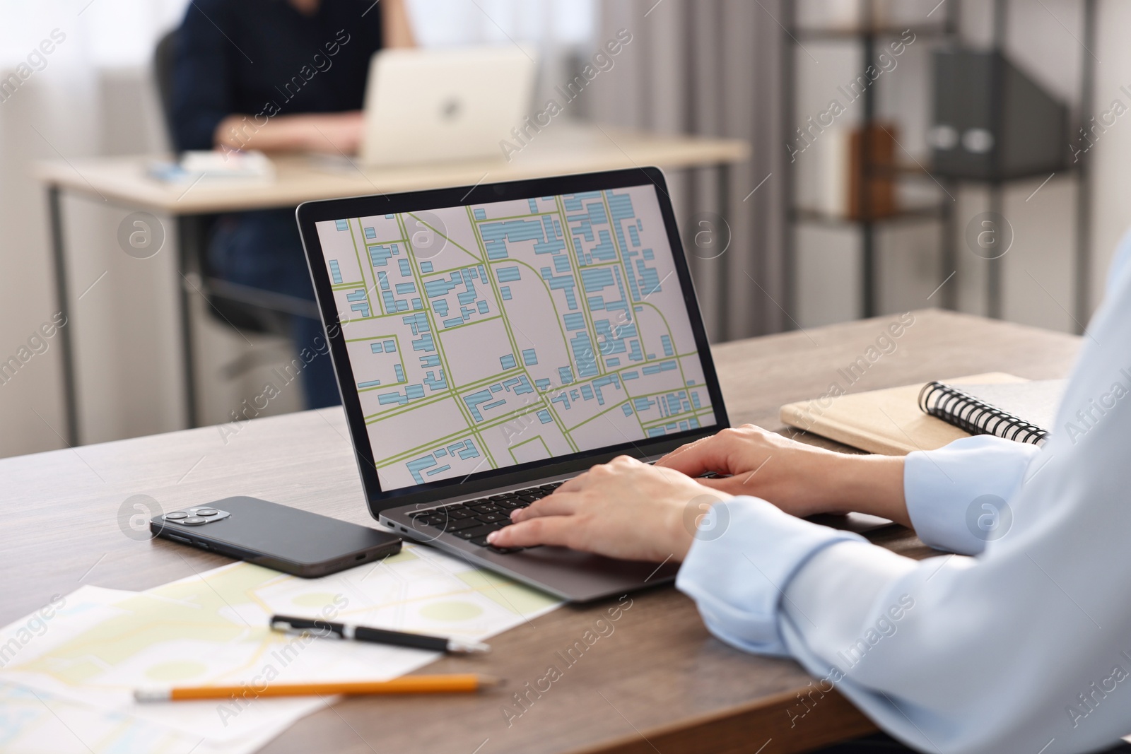 Photo of Cartographer working with cadastral map on laptop at wooden table in office, closeup