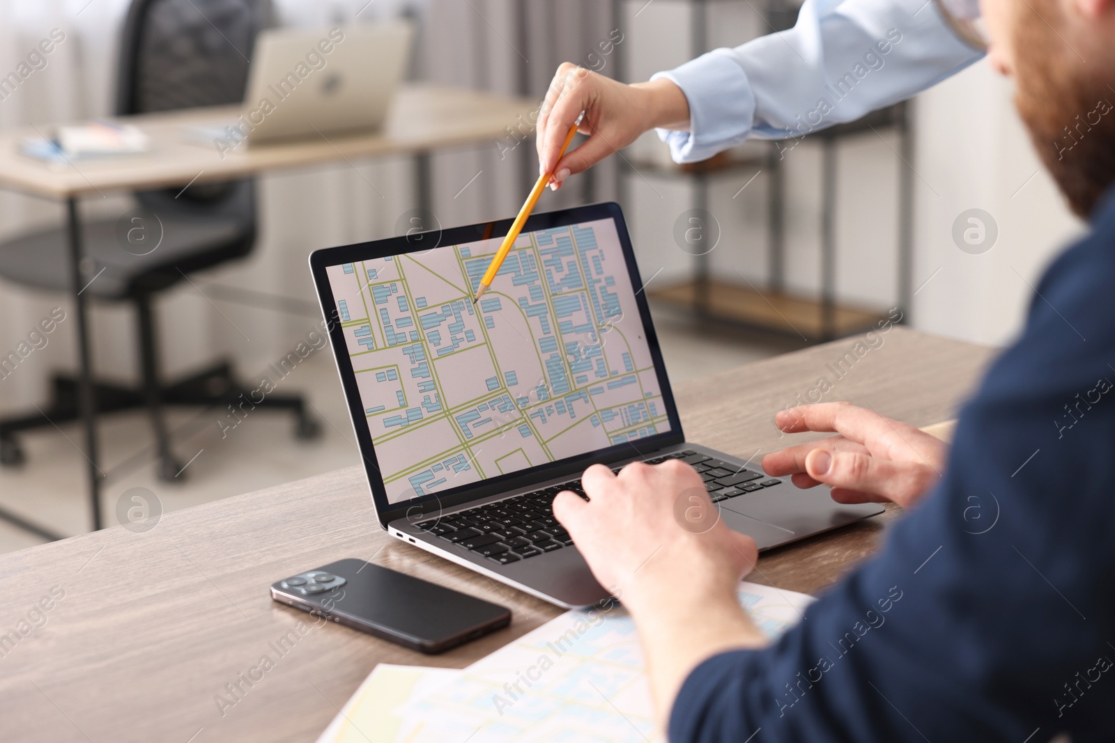 Photo of Cartographers working with cadastral map on laptop at wooden table in office, closeup