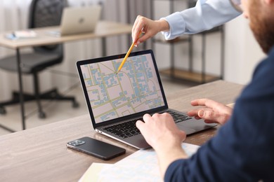 Photo of Cartographers working with cadastral map on laptop at wooden table in office, closeup