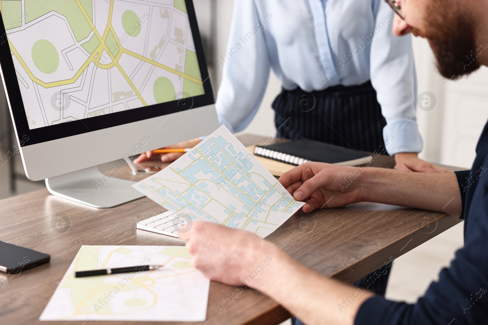 Photo of Cartographers working with cadastral maps at wooden table in office, closeup