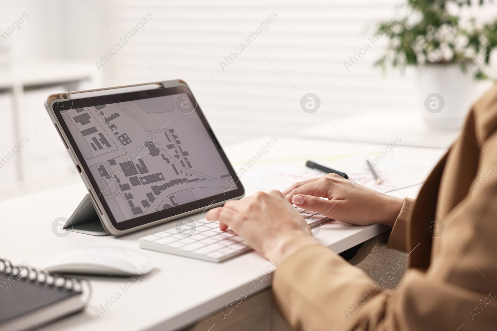 Photo of Cartographer working with cadastral map on tablet at white table in office, closeup