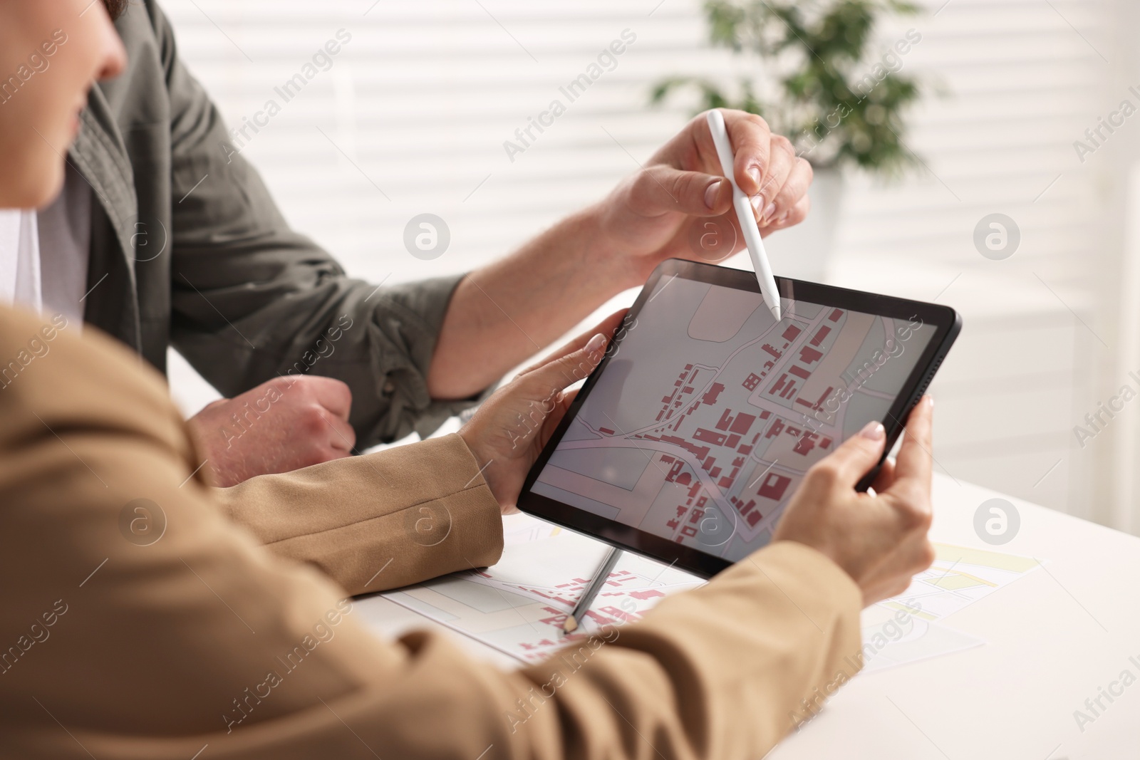 Photo of Cartographers working with cadastral map on tablet at white table in office, closeup