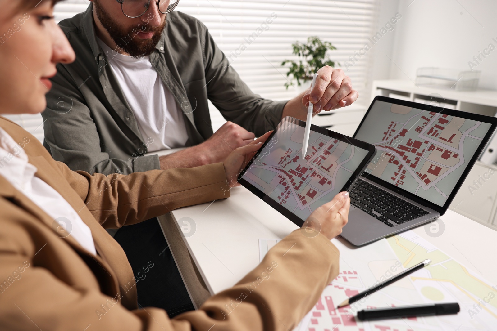 Photo of Cartographers working with cadastral map on tablet at white table in office, closeup