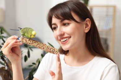 Photo of Woman feeding bright parrot with bird treat indoors, selective focus. Exotic pet