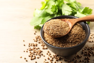 Coriander powder in bowl, spoon, seeds and green leaves on wooden table, space for text