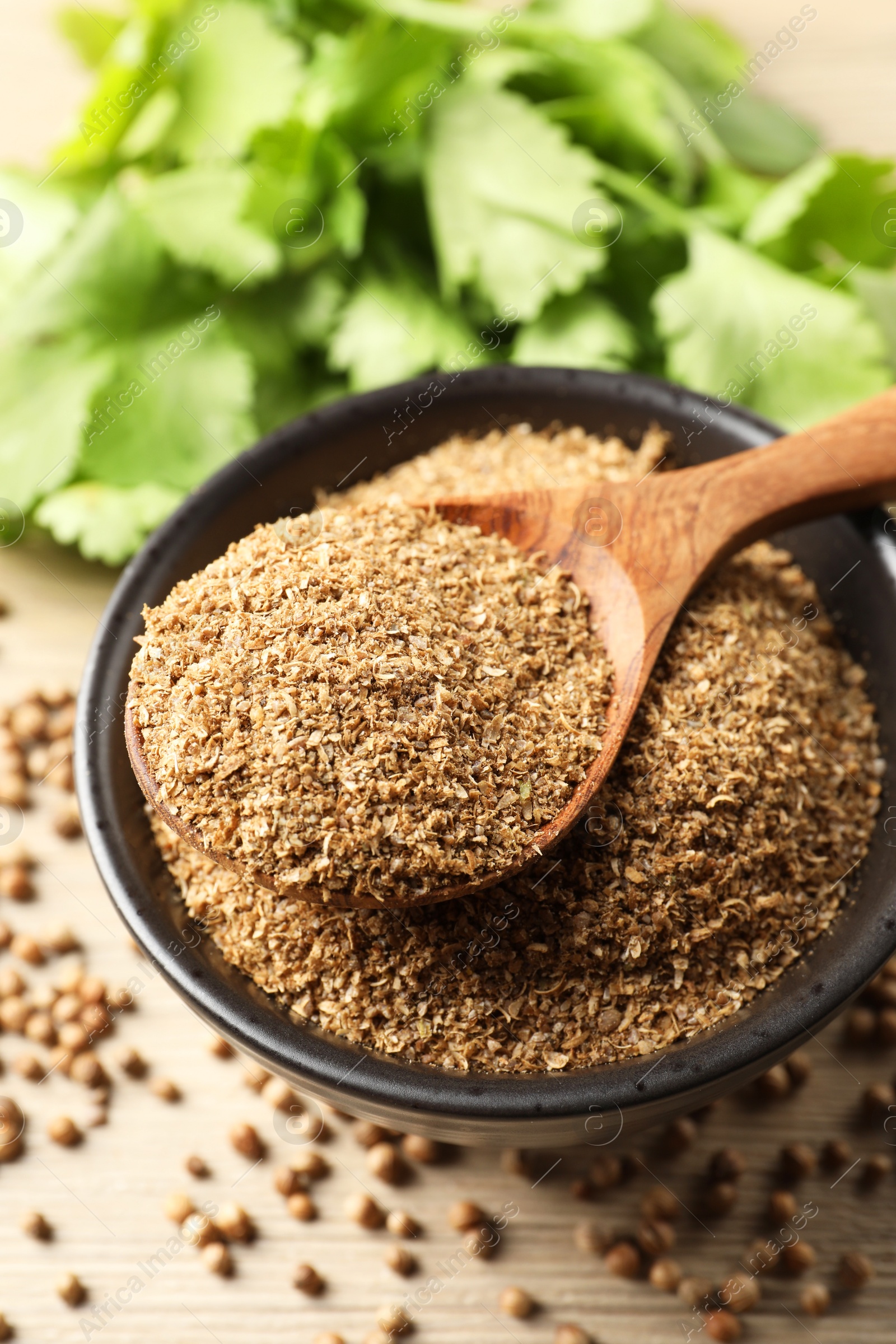 Photo of Coriander powder in bowl, spoon, seeds and green leaves on wooden table