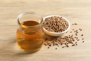 Photo of Dried coriander seeds in bowl and oil on wooden table