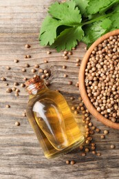 Photo of Coriander essential oil, seeds and green leaves on wooden table, top view