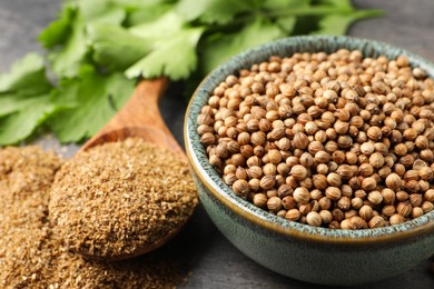 Photo of Dried coriander seeds in bowl, powder and green leaves on table, closeup