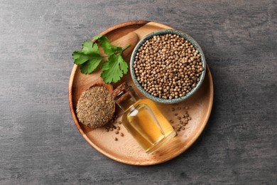 Photo of Coriander essential oil, seeds, powder and green leaves on grey table, top view