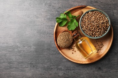 Photo of Coriander essential oil, seeds, powder and green leaves on grey table, top view. Space for text