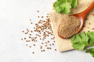 Photo of Coriander powder in spoon, seeds and green leaves on light grey table, top view. Space for text