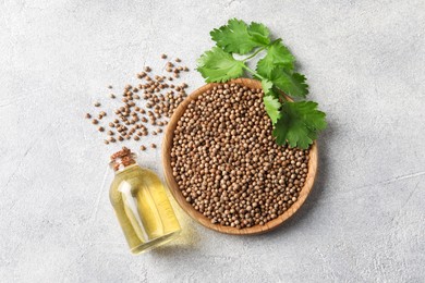 Coriander essential oil, seeds and green leaves on light grey table, top view