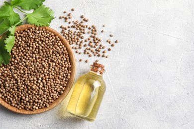 Coriander essential oil, seeds and green leaves on light grey table, top view. Space for text